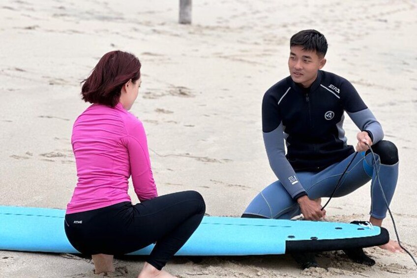 Two people sitting on the beach with a surfboard between them. 3