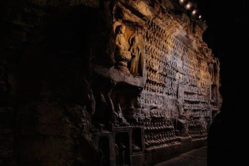A cave with ancient carvings and a seated figure. 5