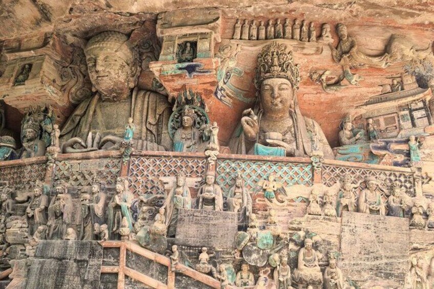 A detailed stone carving with multiple figures, including a central figure in a blue robe, surrounded by smaller figures and intricate patterns. 3