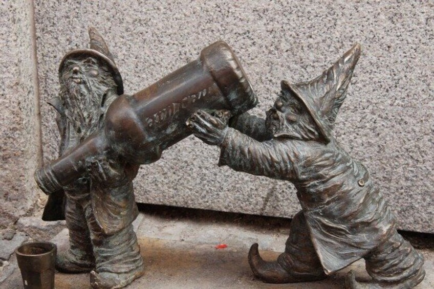 A bronze statue of two figures, one holding a large object, against a stone wall. 3