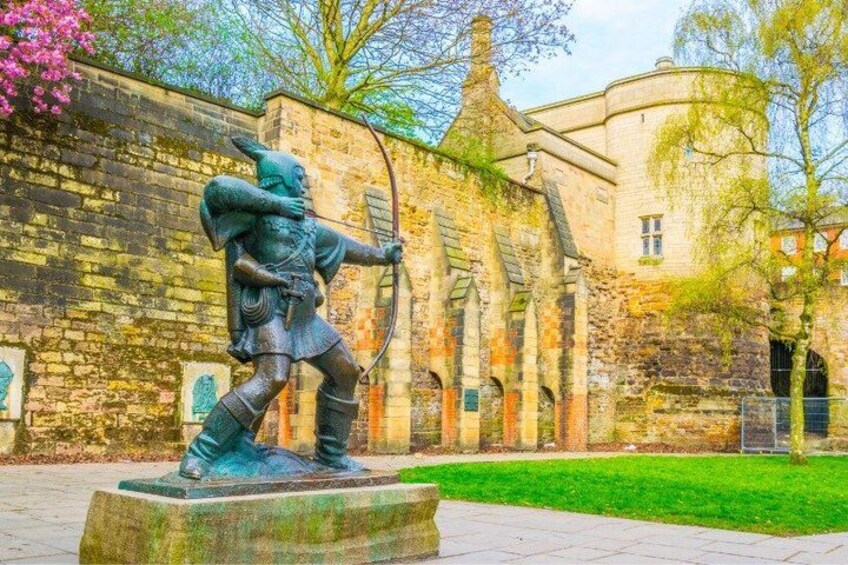 A statue of a knight in armor holding a sword and shield, set against a historic stone building with a green lawn in front. 4