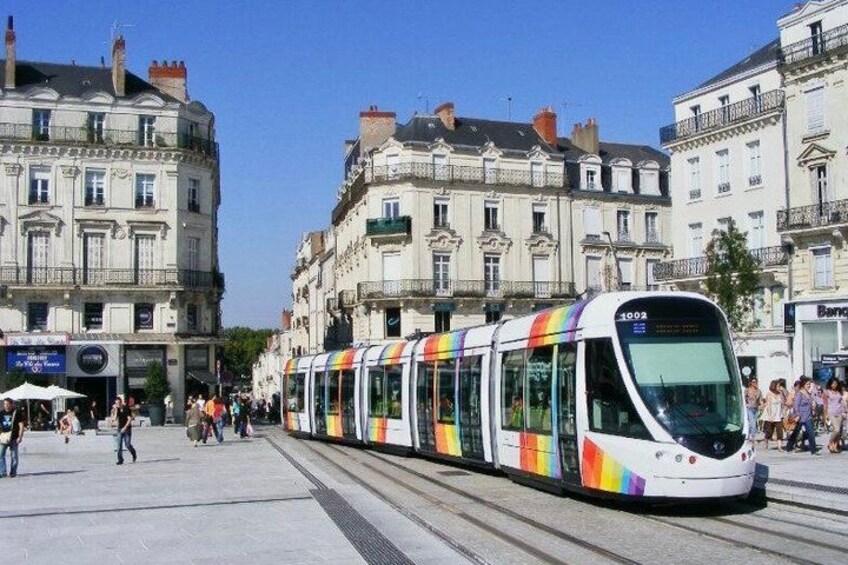 A modern tram with a rainbow design, traveling on a track in an urban area with historic buildings. 1
