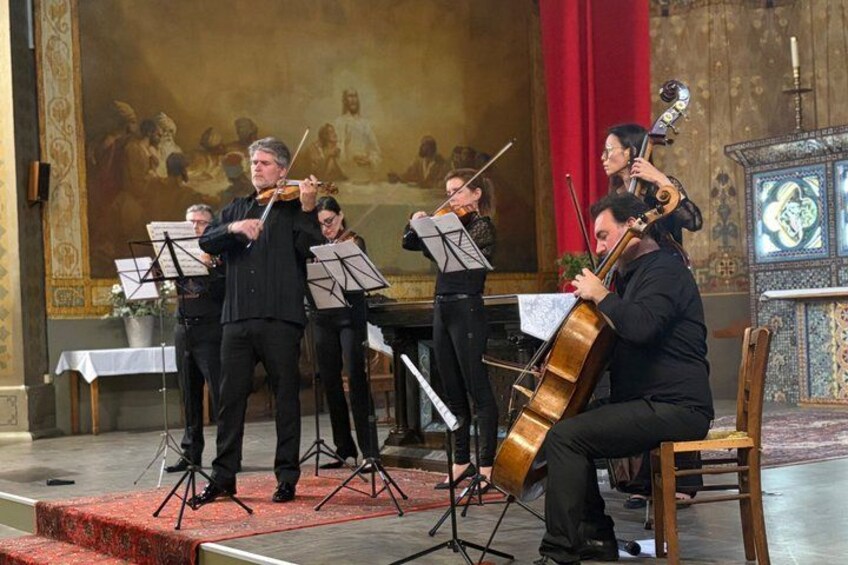 A string quartet performing in a church with a large religious painting in the background. 3
