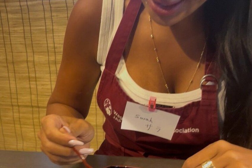 A person wearing a name tag and a red apron, holding a pen. 4