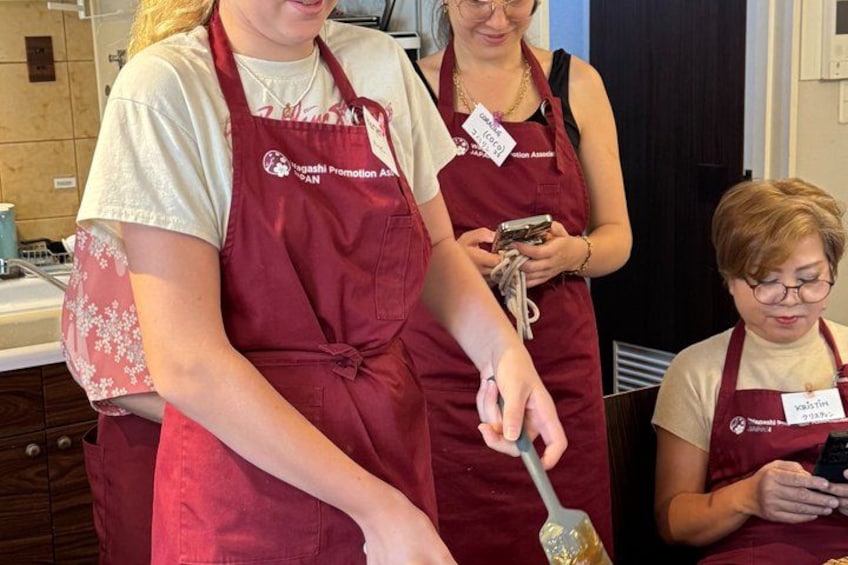 Three people wearing aprons with name tags, engaged in a cooking activity in a kitchen. 2