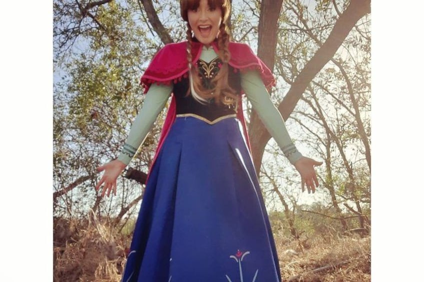 A person in a blue dress with a red cape standing in a wooded area. 2