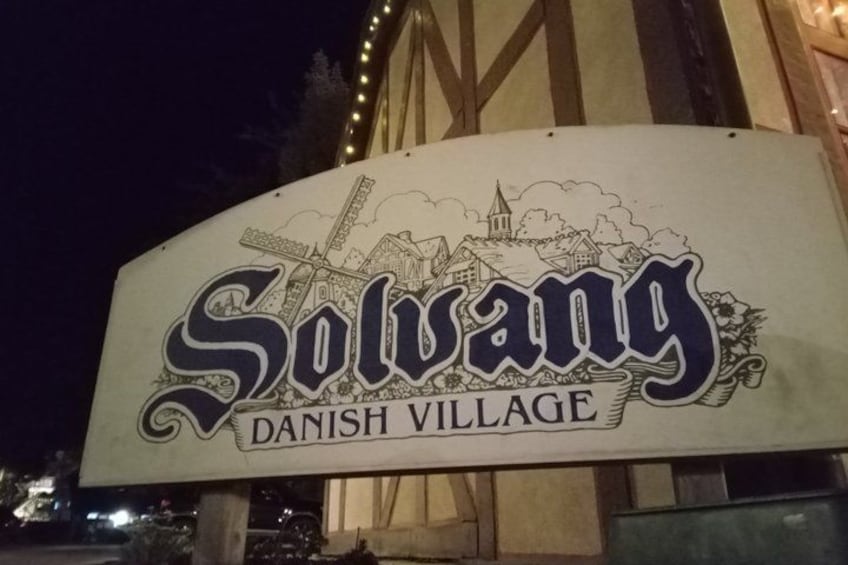 A sign for Solvang Danish Village with a town illustration. 1
