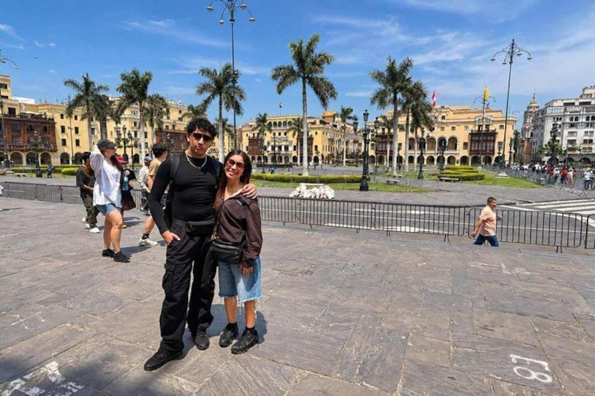 A couple posing in a public square with palm trees and historic buildings in the background. 2