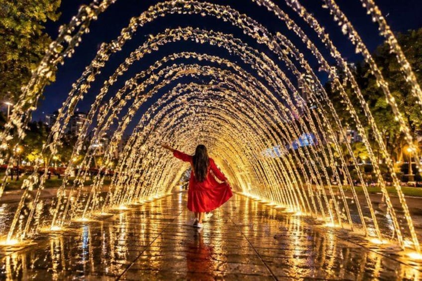 A person in a red dress walking through a water fountain archway at night. 5