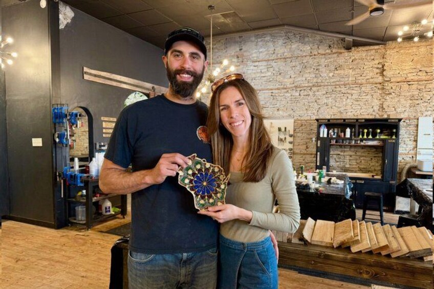 A man and a woman holding a decorative item in a rustic interior with wooden shelves and a brick wall. 1