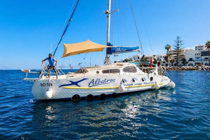 A sailboat named 'Albatros' with a person standing on the deck, sailing on clear blue waters. 1