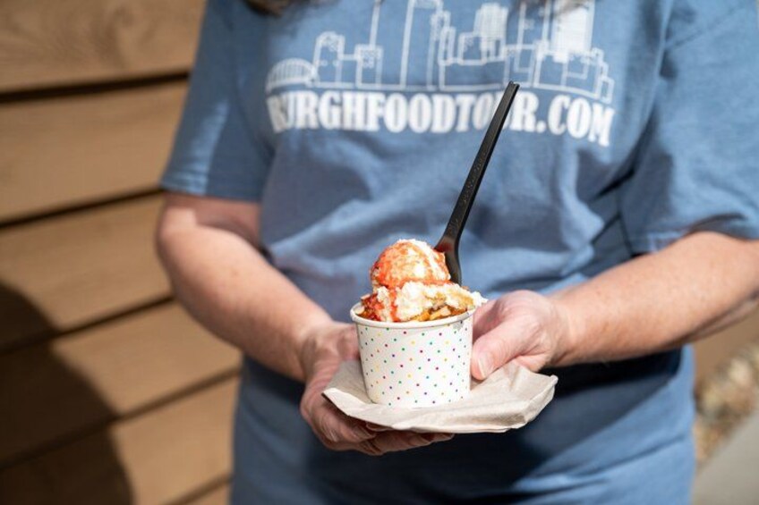 A person holding a cup of ice cream with a black spoon. 2