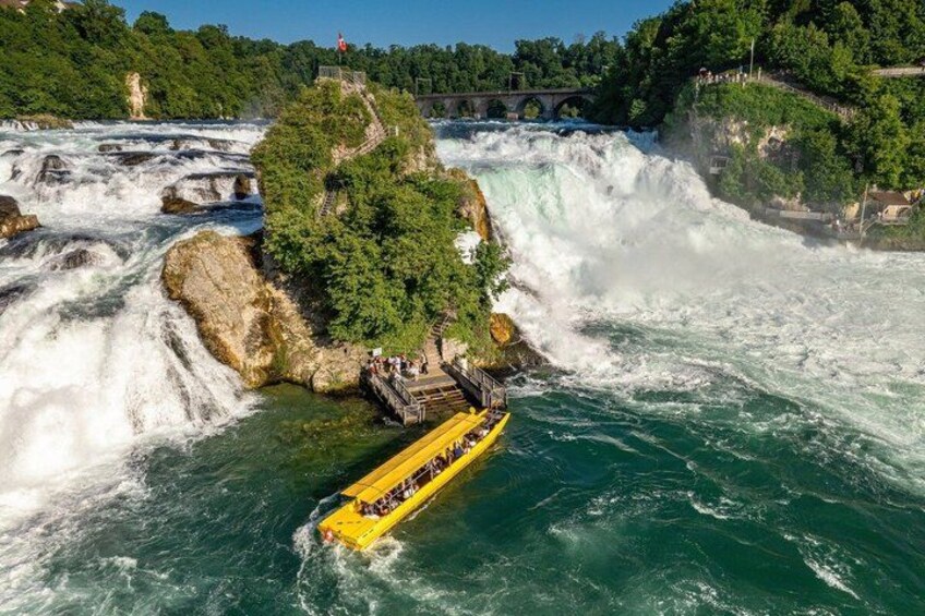 A yellow raft navigating a waterfall, surrounded by lush greenery and a stone bridge in the background. 5