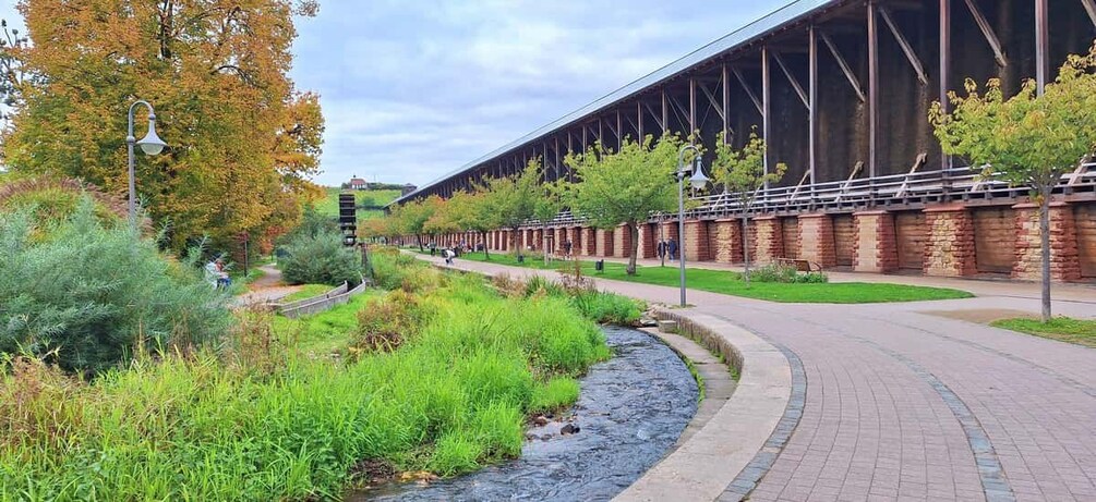 A pedestrian bridge over a river, surrounded by greenery and a brick building. 3
