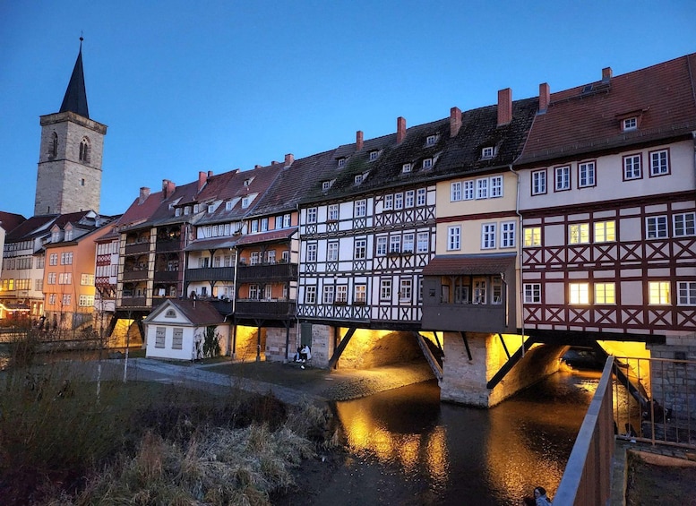 A historic town with half-timbered buildings, a bridge over a river, and a church tower. 1