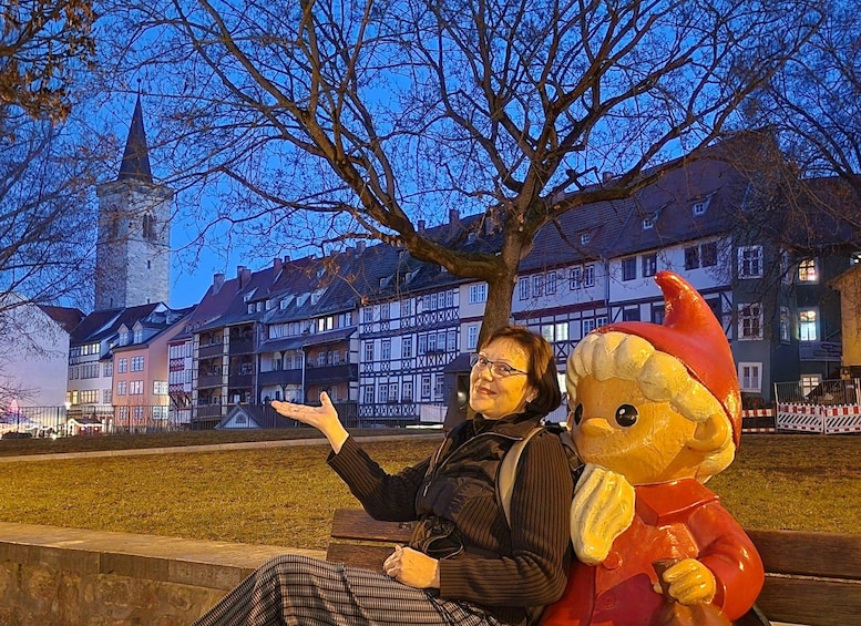 A person sitting on a bench with a large inflatable character nearby. In the background, there are traditional buildings and a tower. 4