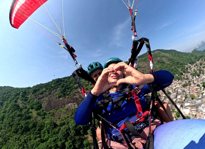 Una persona haciendo parapente con un canopy rojo, usando casco y sosteniendo un palo para tomarse selfies. 4