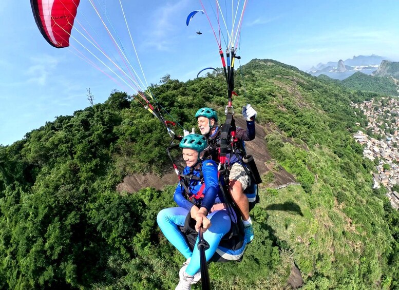 Dos personas practicando parapente sobre un exuberante paisaje verde con una ciudad al fondo. 3