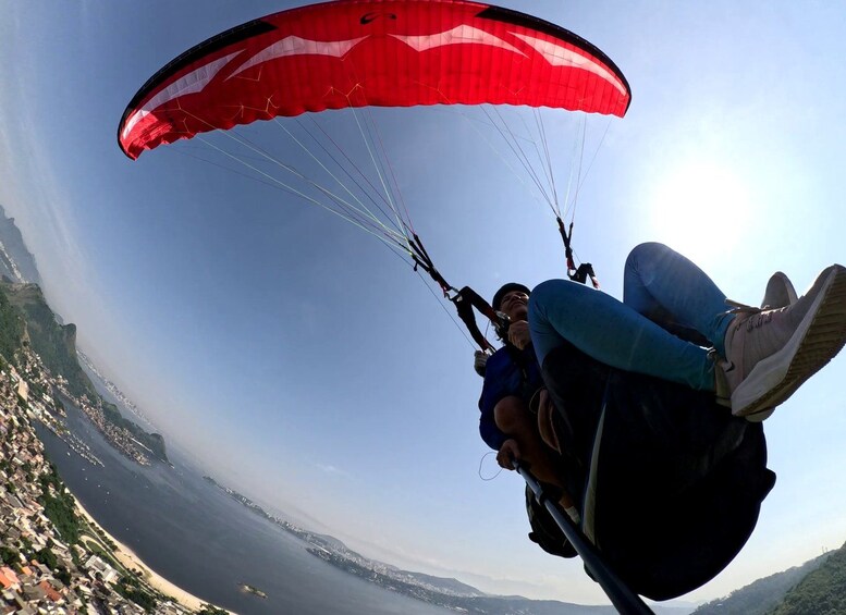 Una persona practica parapente con un paracaídas rojo y blanco, volando sobre una ciudad costera con edificios a la vista y un cielo despejado. 2