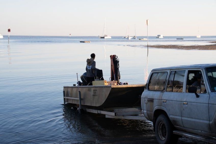 A boat being towed by a vehicle on a calm body of water with several sailboats in the background. 3