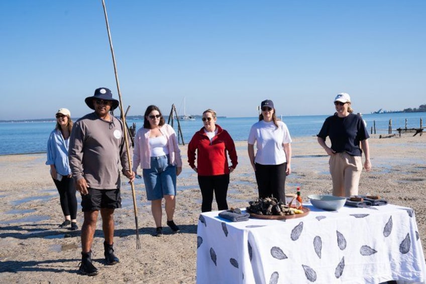 A group of people standing on a beach with a table displaying food items. 1