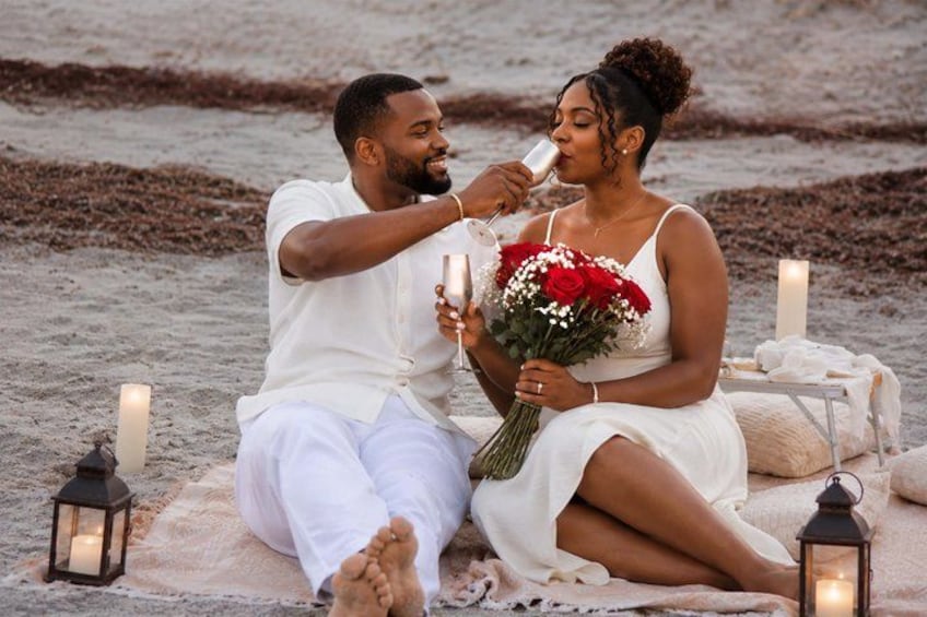 A couple sitting on a blanket by the beach with candles and flowers. 5