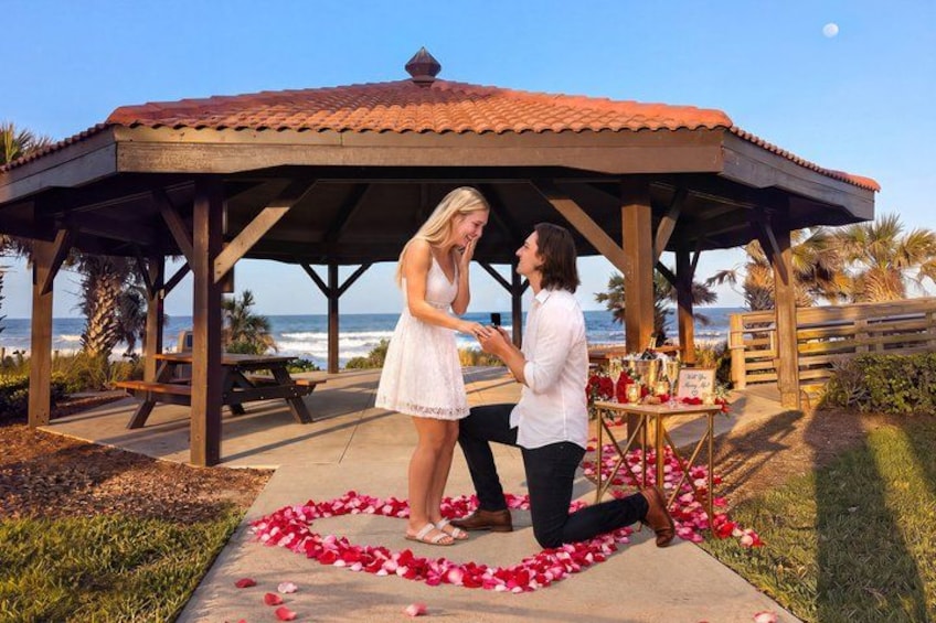 A gazebo, a beach, and a couple with rose petals on the ground. 1