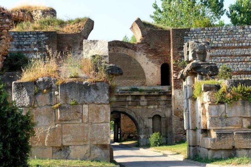 An ancient stone archway with overgrown vegetation, surrounded by stone walls and a grassy area. 4