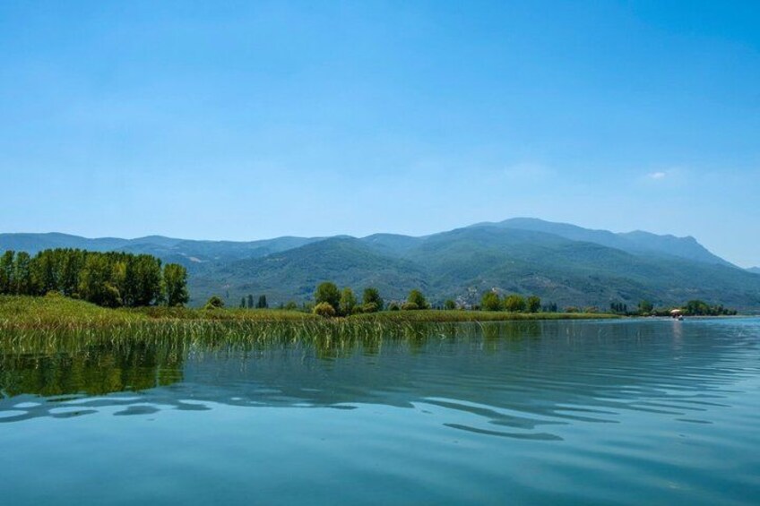 A calm lake with a forested shoreline and distant mountains under a clear sky. 2