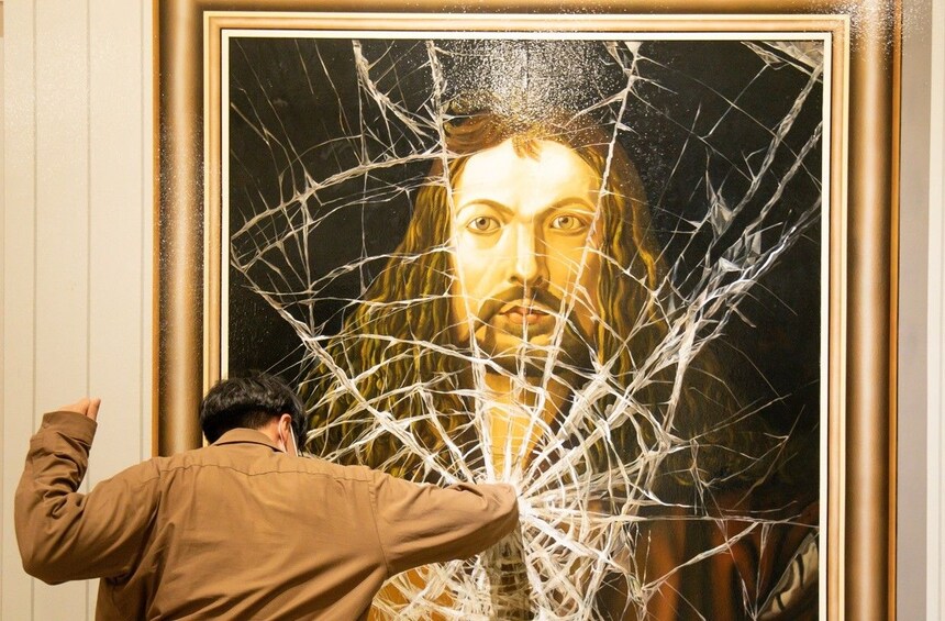 A person standing in front of a large painting with a broken glass window. 3