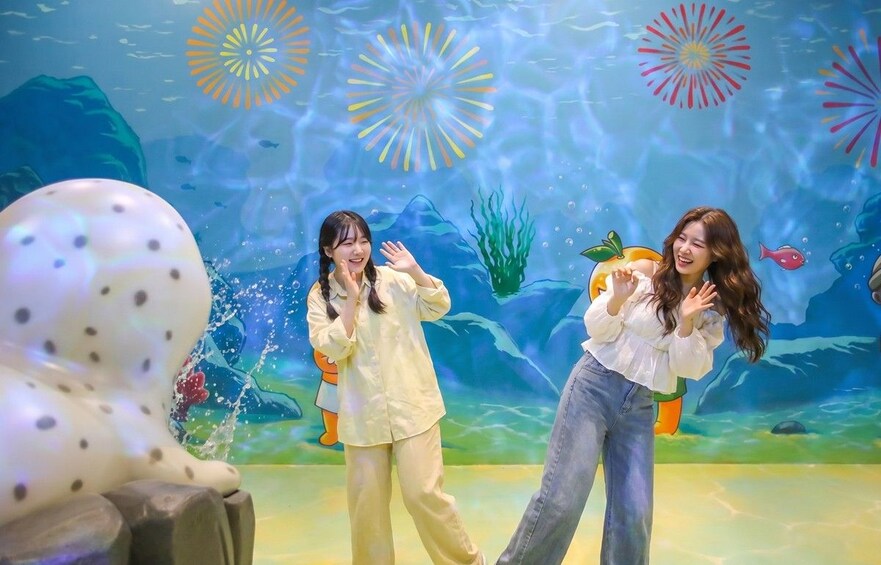 Two people in front of an underwater-themed mural with sea creatures and bubbles. 2