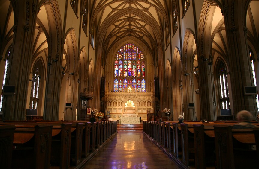 A cathedral interior with a central stained glass window, arched ceilings, and rows of pews. 5