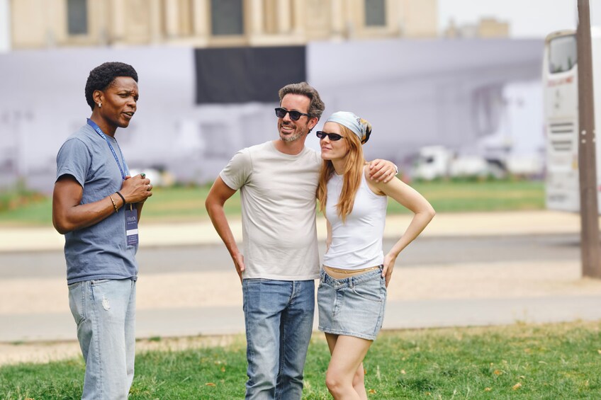Three people standing on grass with a building and a truck in the background. 4