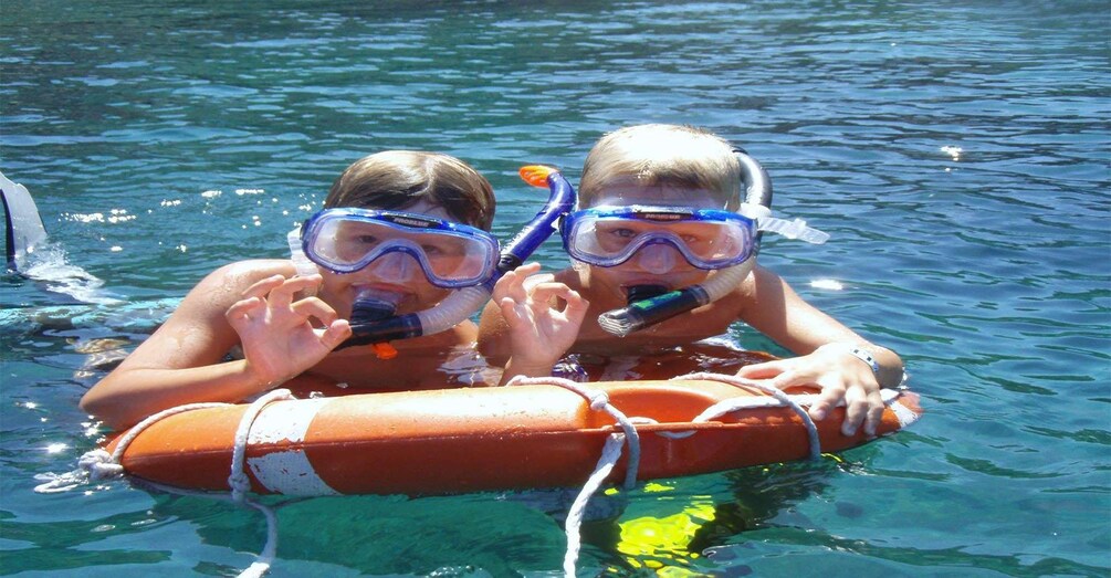 Dos personas haciendo snorkel en agua cristalina y azul, usando chalecos salvavidas naranja y snorkels azules. 4