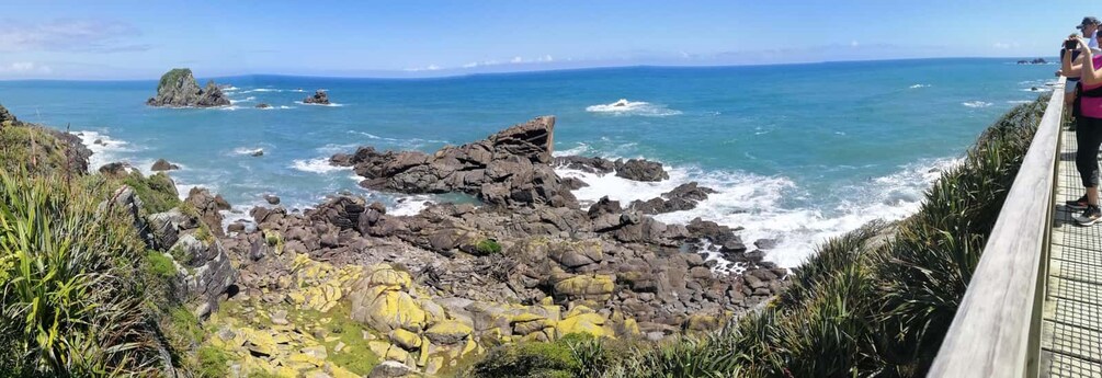 Una costa rocosa con olas rompiendo en la orilla, un muelle de madera y un cielo azul despejado. 4