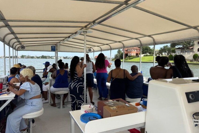 A boat with people on deck, a covered area, and a body of water in the background. 2