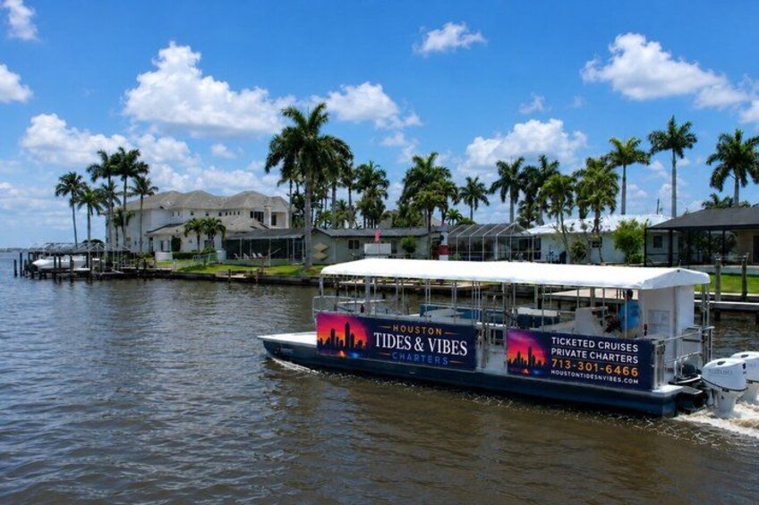 A boat with 'Tides & Vibes' and 'Houston Tides & Vibes Charters' on its side, docked near a waterfront with palm trees and houses. 1