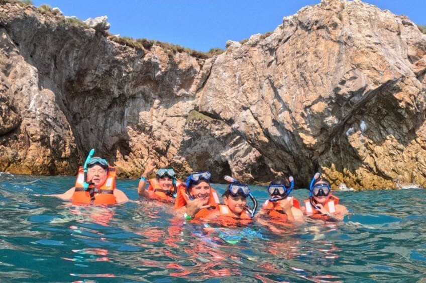 A group of people snorkeling in clear blue water with rocky cliffs in the background. 3