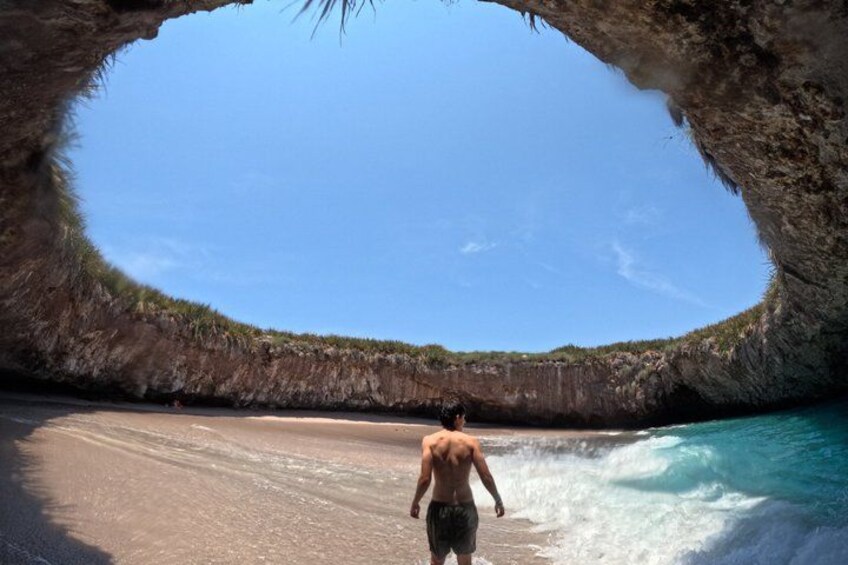 A man walking on a beach with a large rock formation overhead. 5