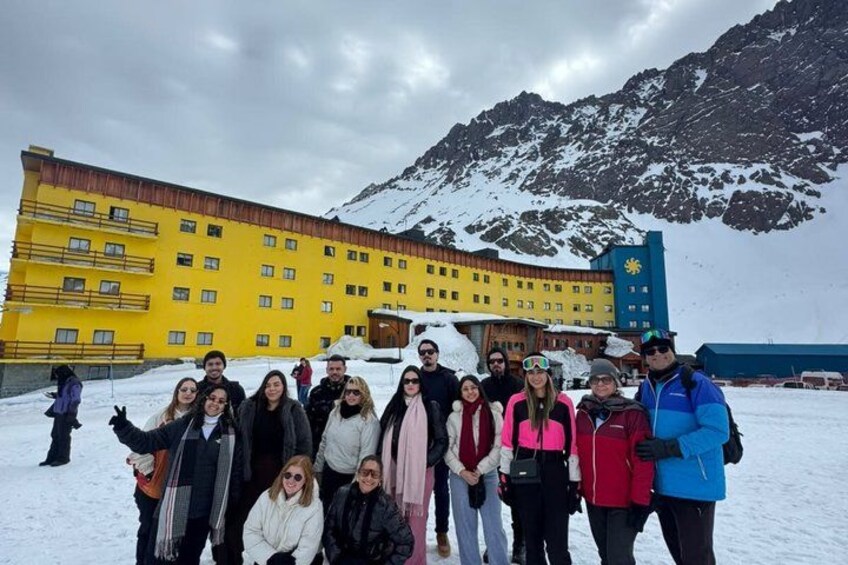 A group of people posing in front of a yellow building with a mountainous backdrop. 4
