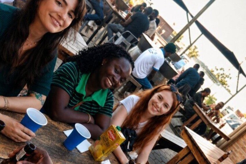 Three people sitting at an outdoor table with cups and a bottle. 3