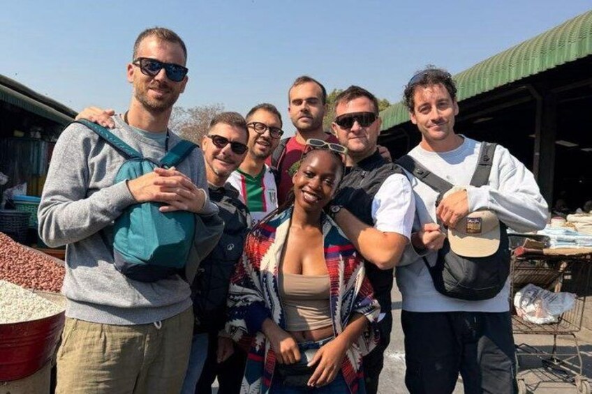 A group of people at an outdoor market with various goods displayed. 1
