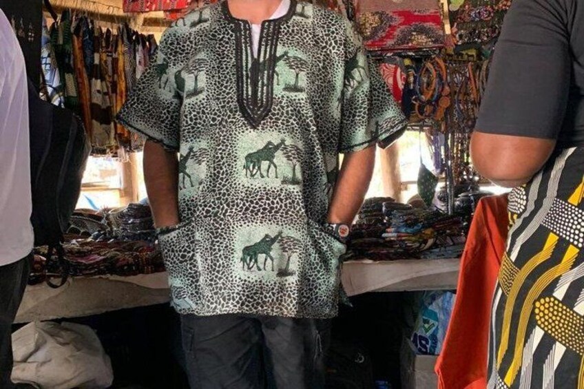 A person wearing a patterned shirt with animal prints, standing in a market with various items on display. 5