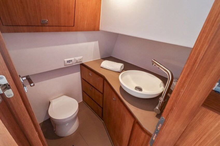 A compact bathroom with a white toilet, wooden cabinets, and a white sink. 2