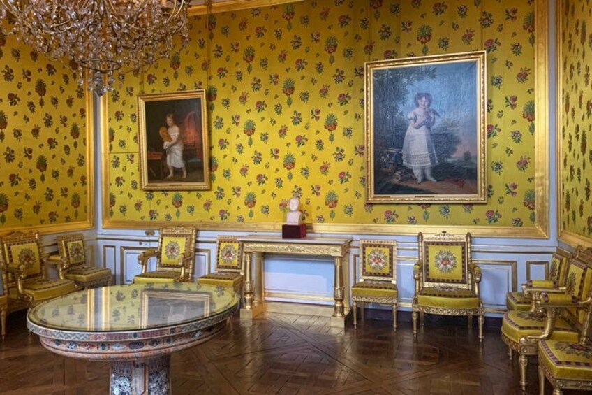 A room with ornate furniture, floral wallpaper, and two framed paintings. 5