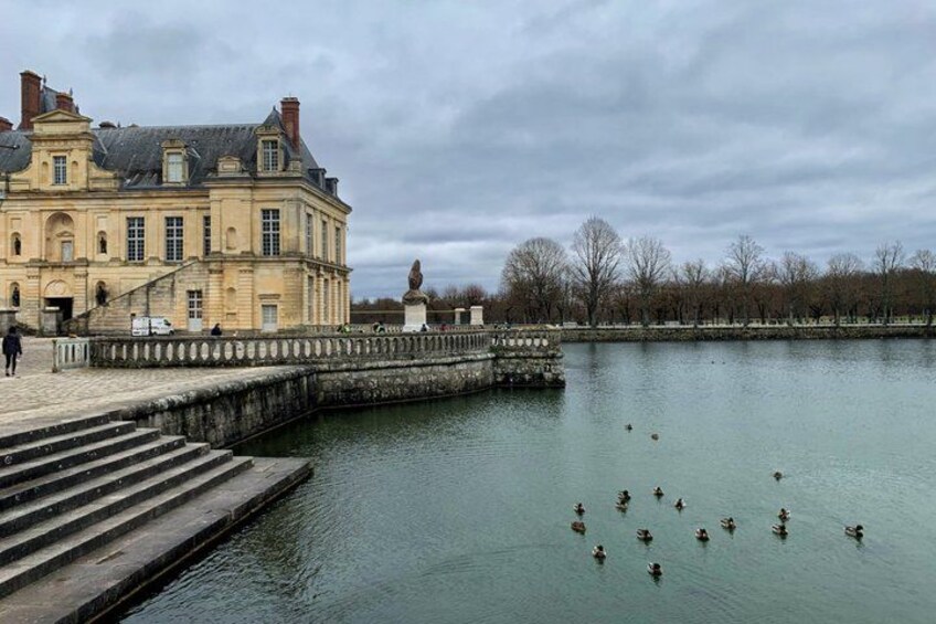 A historic building by a calm water body with ducks swimming. 4