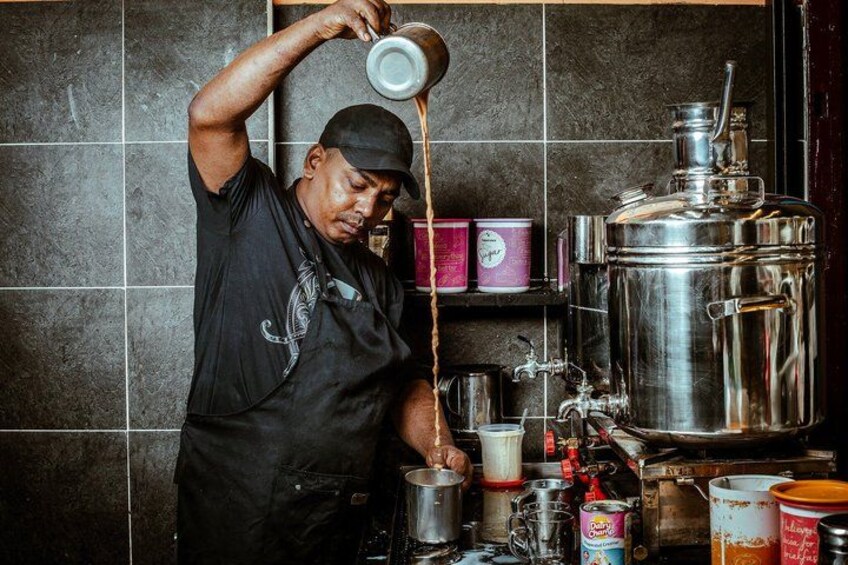 A person pouring a liquid into a container in a kitchen with tiled walls, stainless steel pots, and various kitchen items. 5