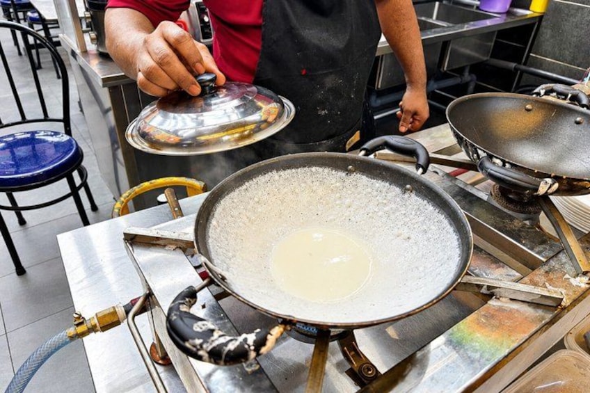 A person cooking with a large wok on a stove, a blue chair, and a metal table in the background. 3