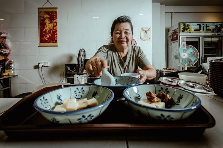 A person serving food from a tray with two bowls, a kitchen counter, and a refrigerator in the background. 1