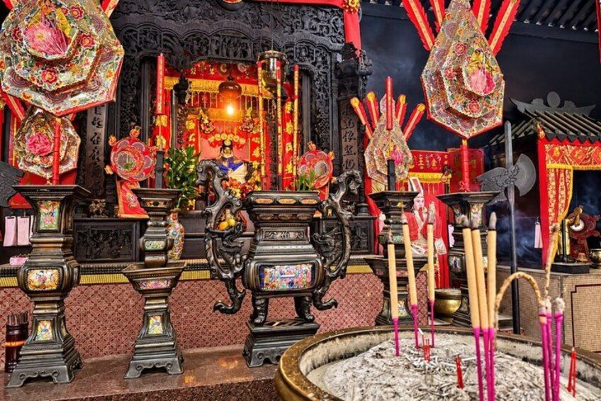 A traditional Chinese altar with incense burners, red decorations, and a statue. 5